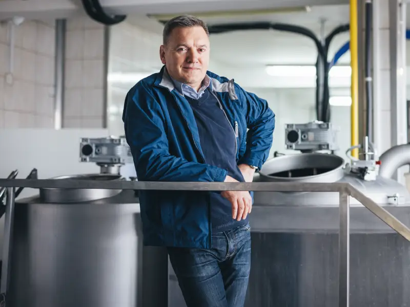 Photo of a male craft brewery owner leaning on the brewing equipment in the brewery.